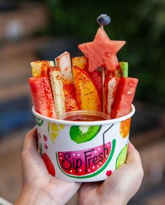 a person holding up a cup filled with watermelon and starfruit sticks