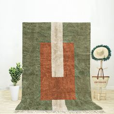 a green and brown rug sitting on top of a wooden floor next to a potted plant