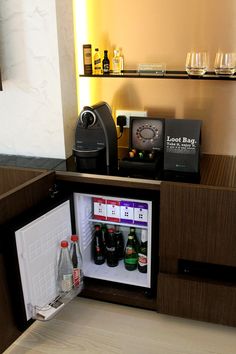 an open refrigerator with drinks in it sitting next to a shelf filled with bottles and glasses