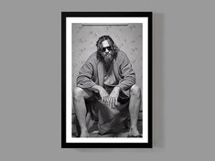 a black and white photo of a man with long hair sitting in front of a wall