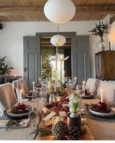 a dining room table set for christmas with candles and apples on the placemats