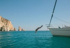 a man dives into the ocean from a sailboat in front of an island