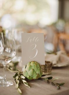 a table number with an artichoke on it and two wine glasses next to it