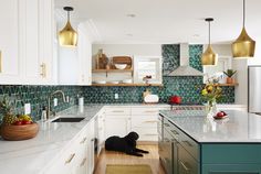 a black dog sitting in the middle of a kitchen with white cabinets and green backsplash