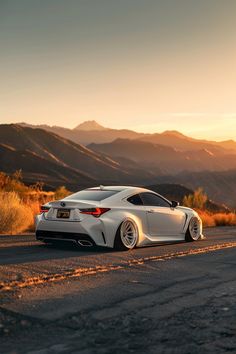 the white car is parked on the side of the road in front of some mountains