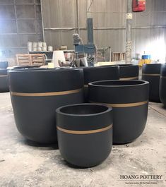 four black pots sitting on top of a floor in front of a metal structure with gold stripes