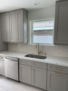 a kitchen with gray cabinets and white counter tops, gold pulls on the faucet