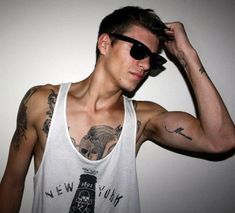 a young man with tattoos on his arms and shoulder, wearing a white tank top