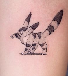 a small black and white cat tattoo on the thigh, with an arrow in it's tail