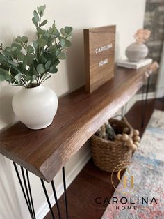 a wooden shelf with metal hairpinks and a white vase on it, next to a sign that says carolina home