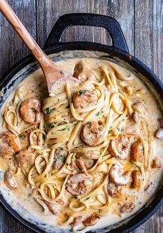 a skillet filled with shrimp and pasta on top of a wooden table next to a spatula