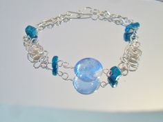 Blue beaded wire bracelet. It measures approx. 7 inches long and has a hook closure. Made with a round cornflower blue glass cabochon in the center, 4 deep turquoise blue glass square beads and swirling Peruvian Alpaca Silver wire chain. Handmade, delicate and light weight. Add it to your jewelry wardrobe. All sales are final and as is. Thank you for looking. You may also love this: https://www.etsy.com/listing/236165636/red-murano-glass-tear-drop-earrings-hoop?ga_search_query=murano&ref=sho Modern Turquoise Glass Jewelry, Blue Wire Wrapped Bracelets With Round Beads, Blue Wire Wrapped Bracelet With Round Beads, Turquoise Czech Glass Round Jewelry, Czech Glass Bracelet With Lobster Clasp, Blue Wire Wrapped Bracelets, Blue Glass Bracelet Jewelry, Unique Blue Wire-wrapped Bracelets, Turquoise Glass Round Jewelry