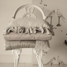 a white chair with pillows on top of it in front of a wall full of birds