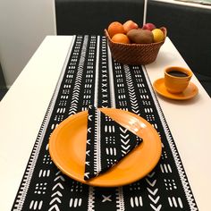 a table topped with an orange and black place mat next to a bowl of fruit