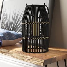 a black birdcage sitting on top of a wooden table next to a pillow