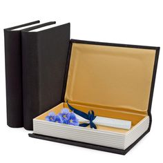 an open book with blue flowers in it next to two black books on a white background