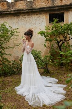 a woman in a white dress is standing near an old building and looking at her cell phone