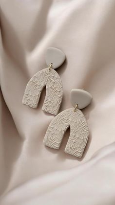 two pairs of white earrings sitting on top of a bed next to a beige sheet