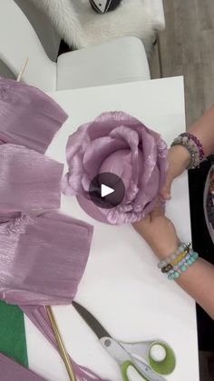 a person cutting fabric with scissors and a flower on top of the table in front of them