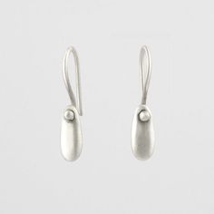 two silver earrings are hanging from hooks on a white surface, one has a ball and the other is a drop