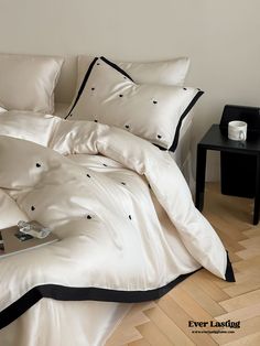 a bed with white sheets and black trim on the headboard is next to a small table