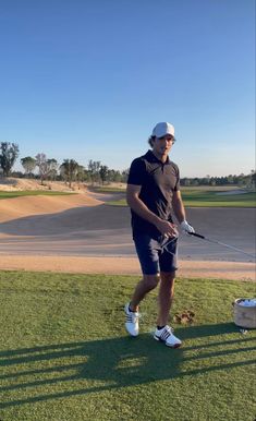 a man holding a golf club on top of a green grass covered field next to a white bucket