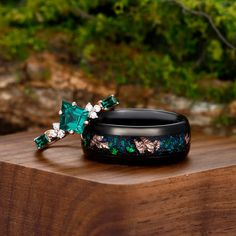 two rings with green and white stones on top of a wooden table next to trees