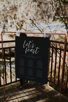 a sign that says let's feast on it next to a wooden deck with trees in the background