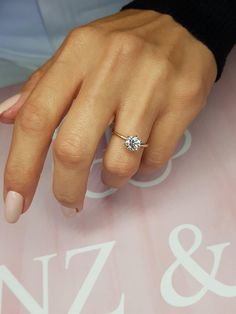 a woman's hand with a diamond ring on her finger and pink nail polish