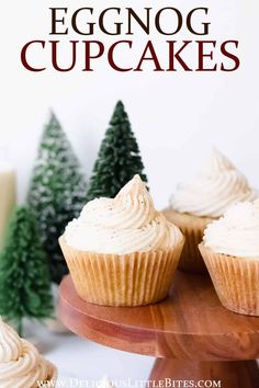 eggnog cupcakes with white frosting on a wooden plate next to christmas trees