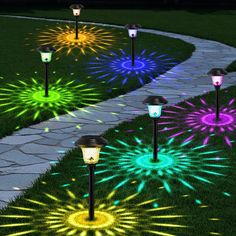 some lights that are on in the grass near a path with flowers and stars around them