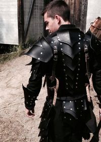 a man in black leather armor walking down a dirt road