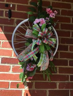 a bicycle wheel hanging on the side of a brick wall with flowers and ribbons tied to it