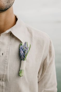 a man wearing a button up shirt with flowers pinned to his lapel, standing next to the water