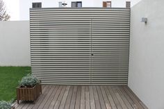 a wooden deck in front of a white wall with vertical slatted panels on it