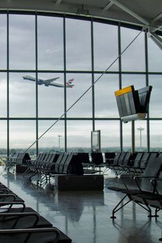 an airport terminal filled with lots of chairs and a plane in the sky behind them