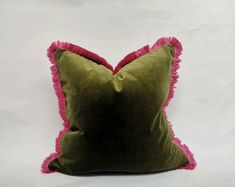 a green pillow with pink fringe trim on it's sides and a white wall in the background