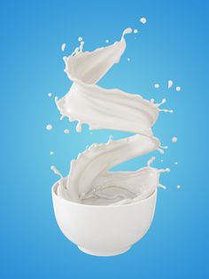 a white bowl filled with milk on top of a blue background and falling into the air