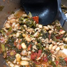 a pot filled with beans and greens next to a spoon