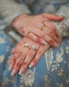 a woman's hands with hennap and rings on her fingers, sitting in a blue dress