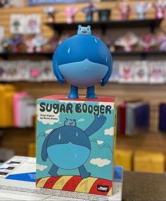 a blue toy sitting on top of a book in a store display case with other toys behind it