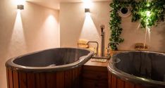 a bathroom with two black bath tubs next to each other and plants growing on the wall