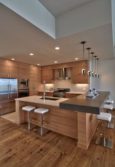 a modern kitchen with wooden floors and stainless steel appliances, including an island countertop