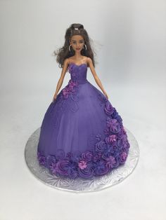 a barbie doll wearing a purple dress on top of a silver cake plate with flowers