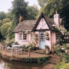 a pink cottage with flowers on the roof and windows next to a body of water