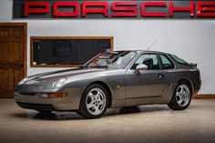 a silver porsche sports car parked in front of a porsche dealership sign with the word porsche on it