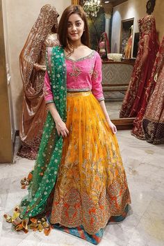 a woman standing in front of a mirror wearing an orange and green lehenga