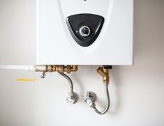 a tankless water heater mounted on the wall with two hoses attached to it