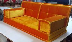 an orange couch sitting on top of a white table next to a red and yellow chair