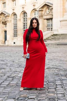 a woman in a long red dress standing on a cobblestone street